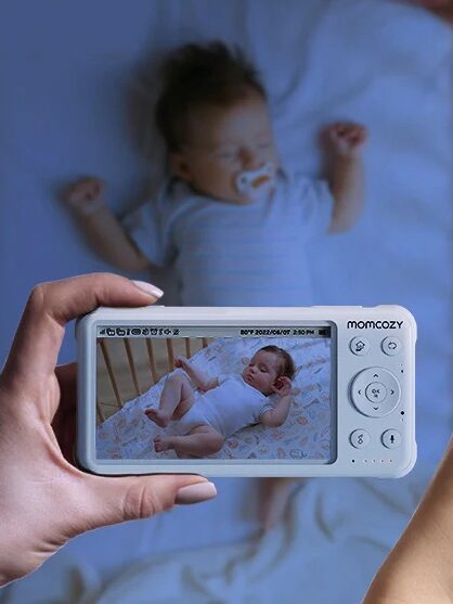 Two hands hold baby monitors displaying live video of babies in cribs; one monitor shows night vision and the other daytime mode—perfect for parents looking for peace of mind between soothing routines or reaching for massage guns to relax.