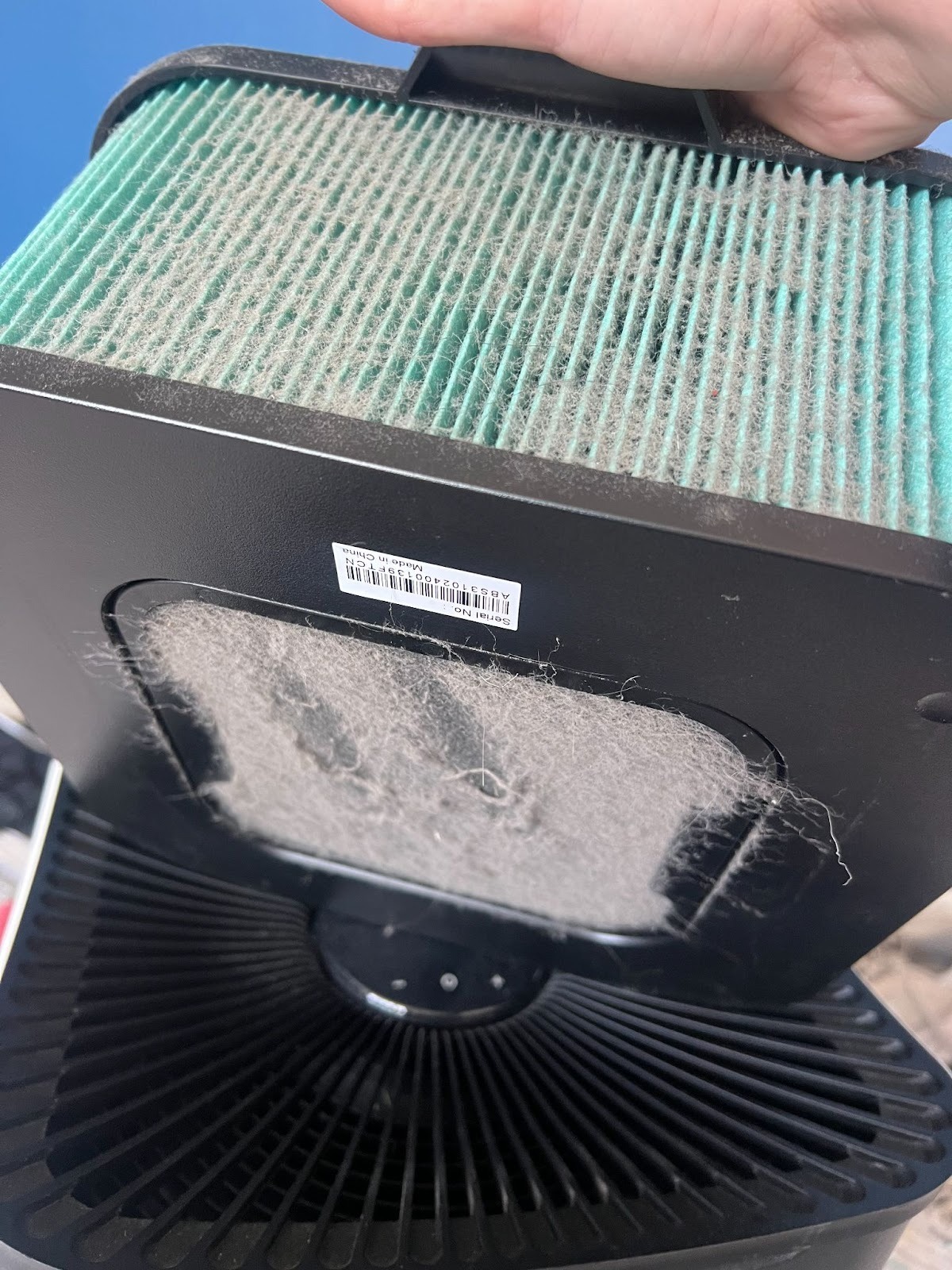 A close-up of a hand holding a HEPA air filter covered in dust, with dust buildup also visible on the housing below.