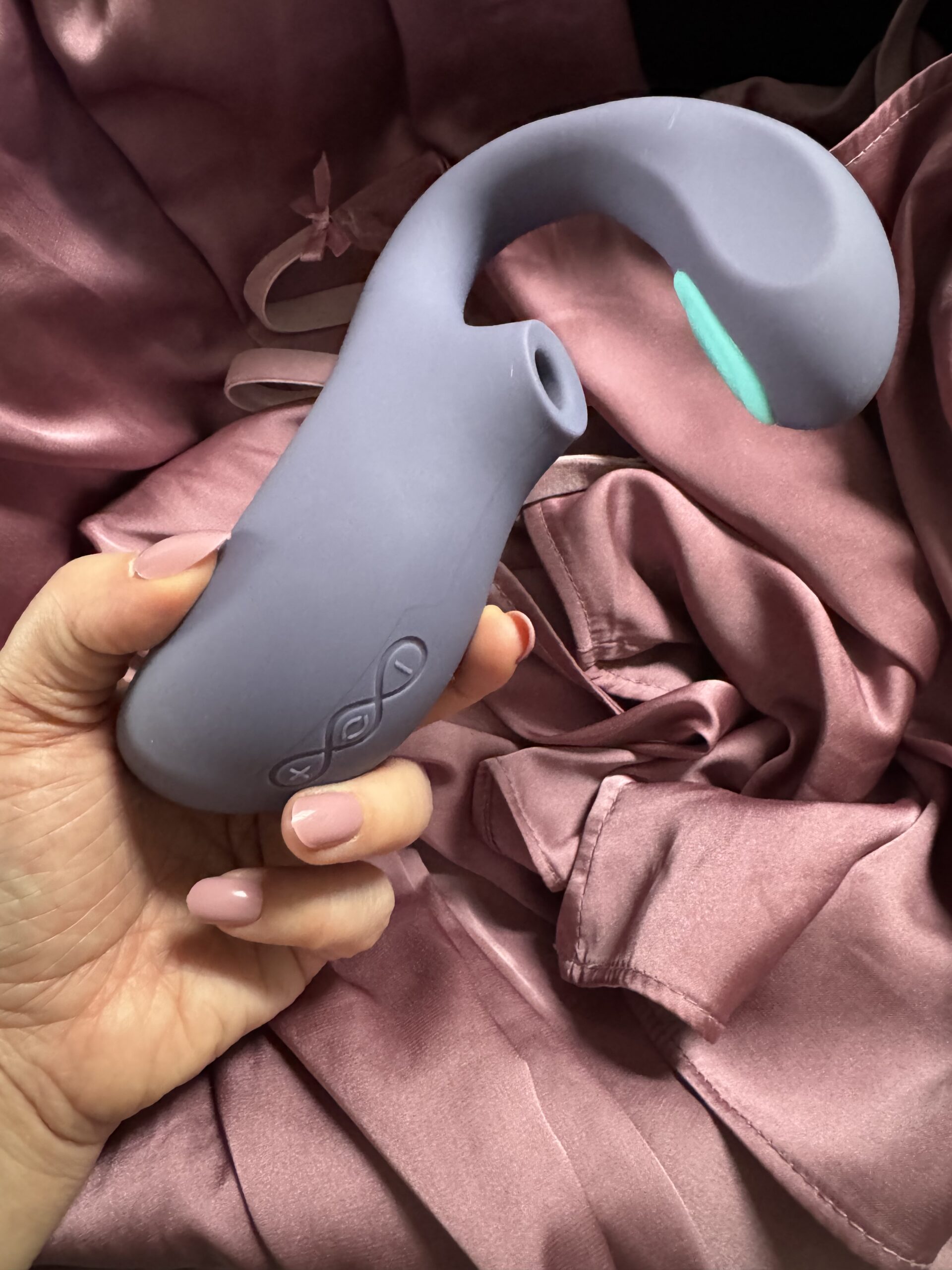 A hand holding a purple silicone sex toy with buttons, shown over a mauve satin fabric background.