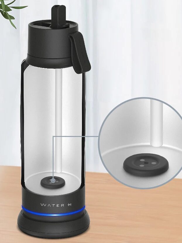 A clear smart waterbottle with a black lid and base sits on a wooden surface; an inset zooms in on a circular device at the bottom inside the bottle.