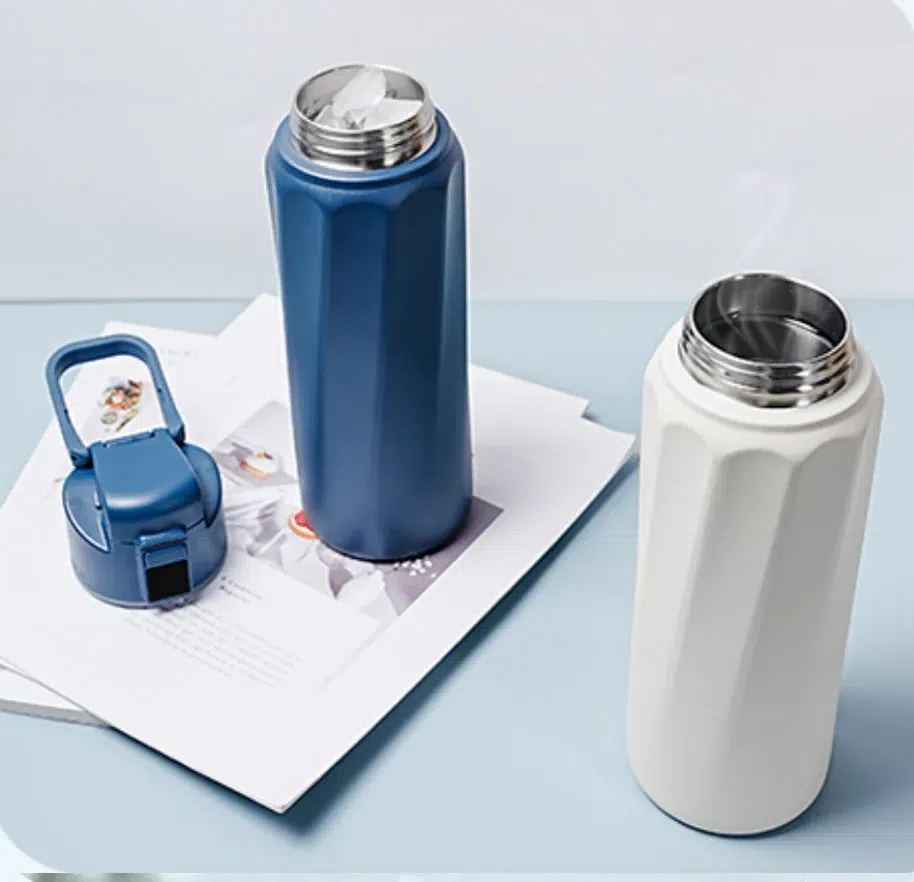 A blue and a white insulated smart waterbottle with fluted designs are shown; the blue bottle's lid is detached and resting on papers beside the bottles.
