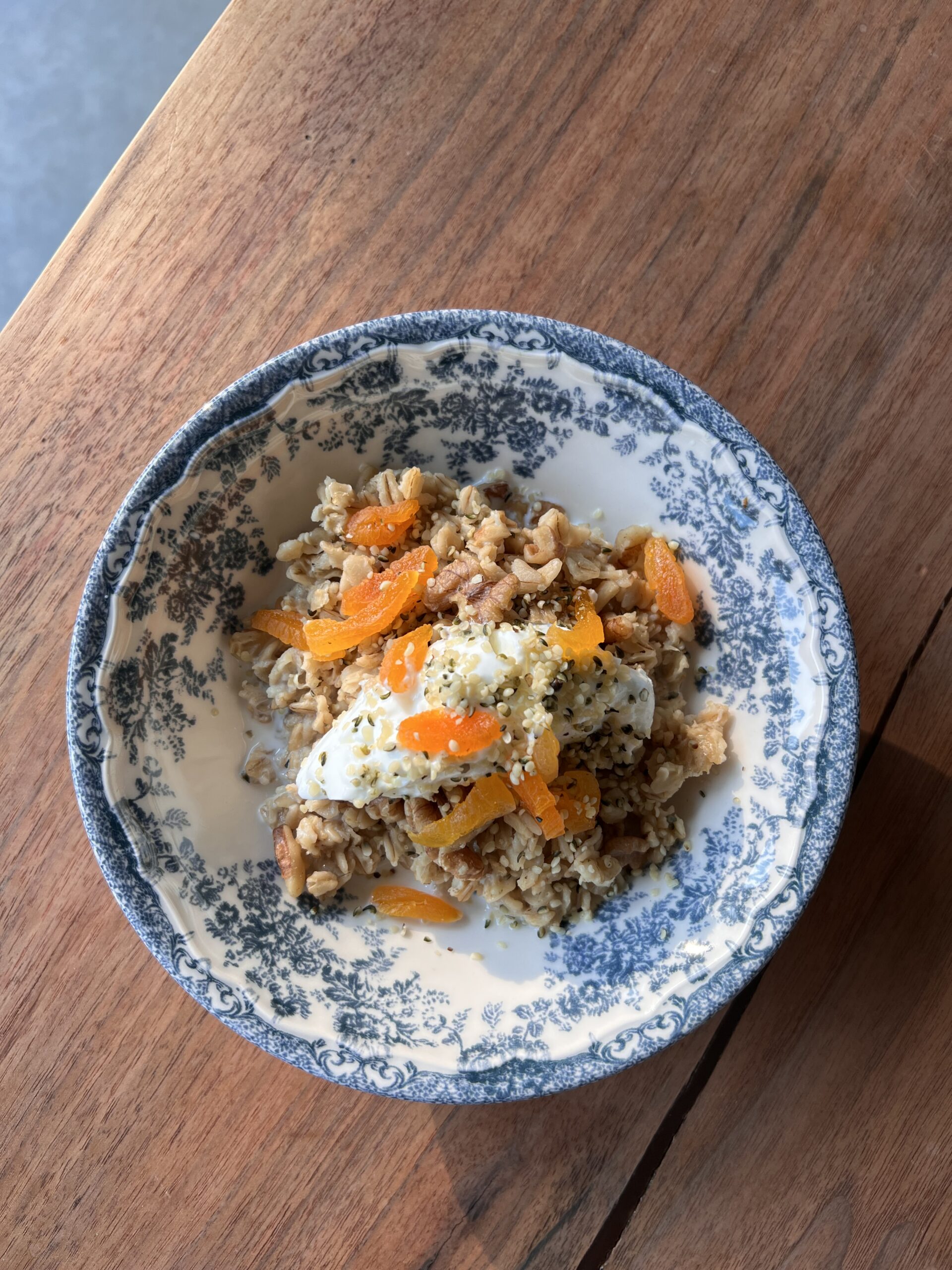 A bowl of oatmeal topped with chopped dried apricots, walnuts, and a dollop of yogurt, served on a wooden table.