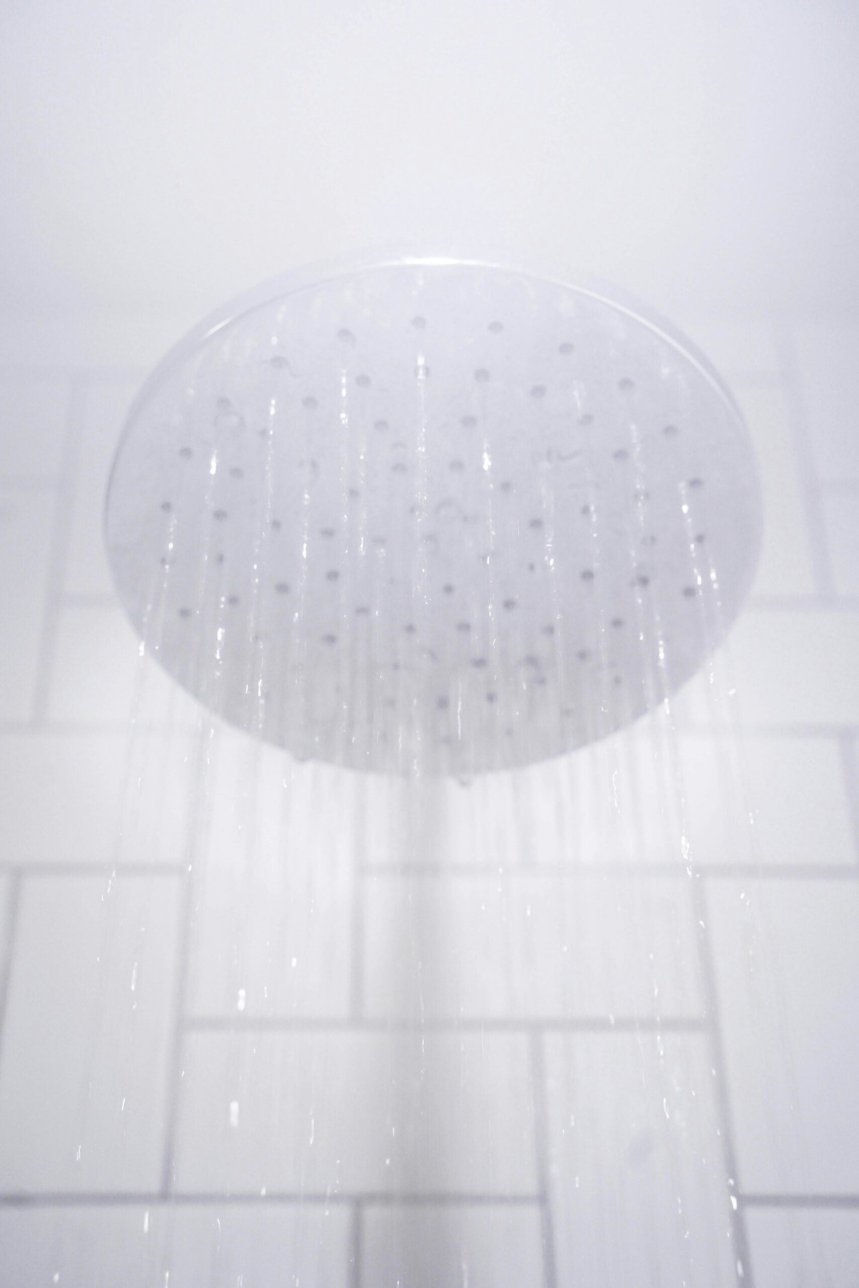 A round showerhead mounted on a tiled wall releases streams of water downwards.