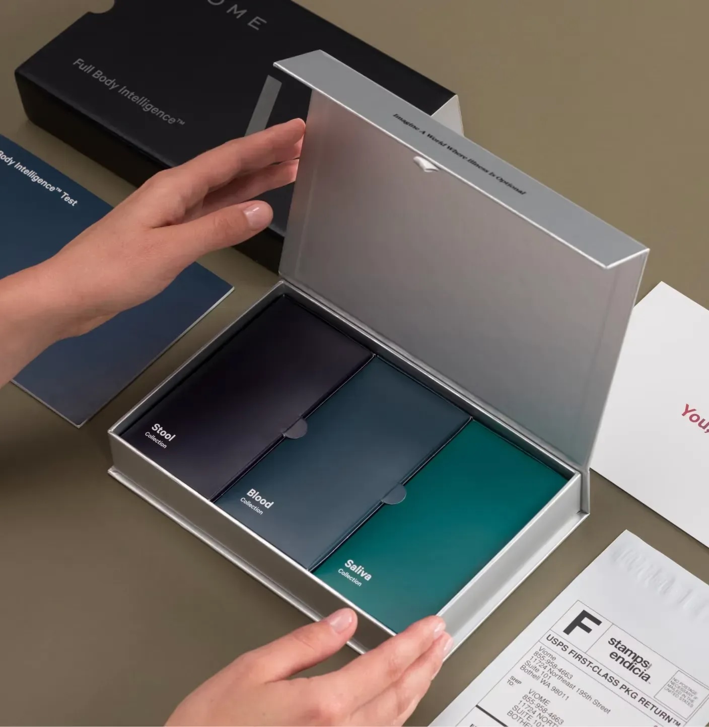 A person opens a box containing three labeled sample kits—Saliva, Blood, and Stool—alongside instructions, packaging materials, and massage guns neatly arranged on the table.