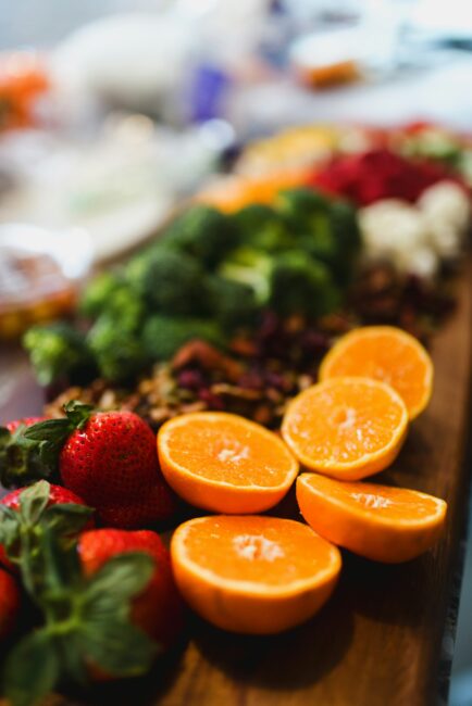 Sliced oranges, strawberries, broccoli, and other vegetables arranged on a wooden board.