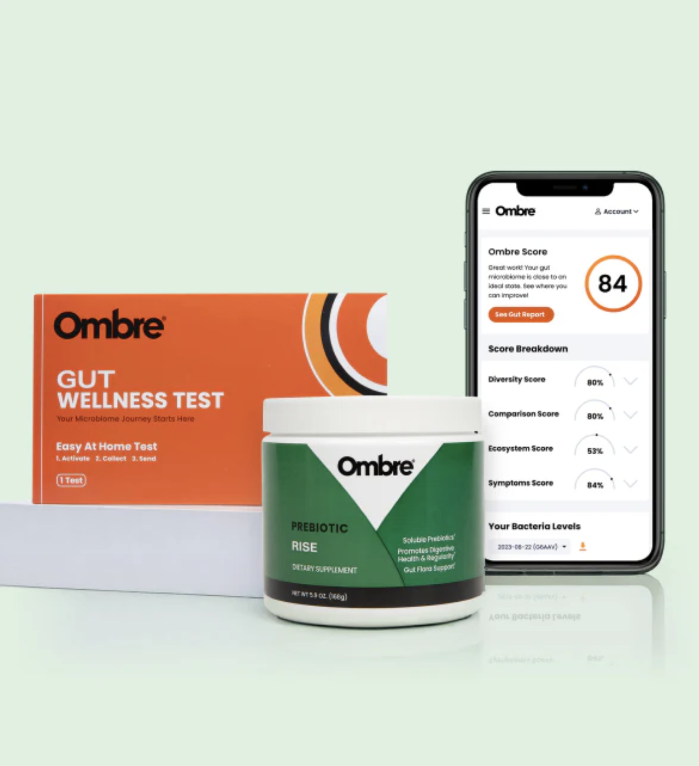 Ombre Gut Wellness Test kit, a container labeled Prebiotic Rise, massage guns in the background, and a smartphone displaying Ombre test results with a score of 84.