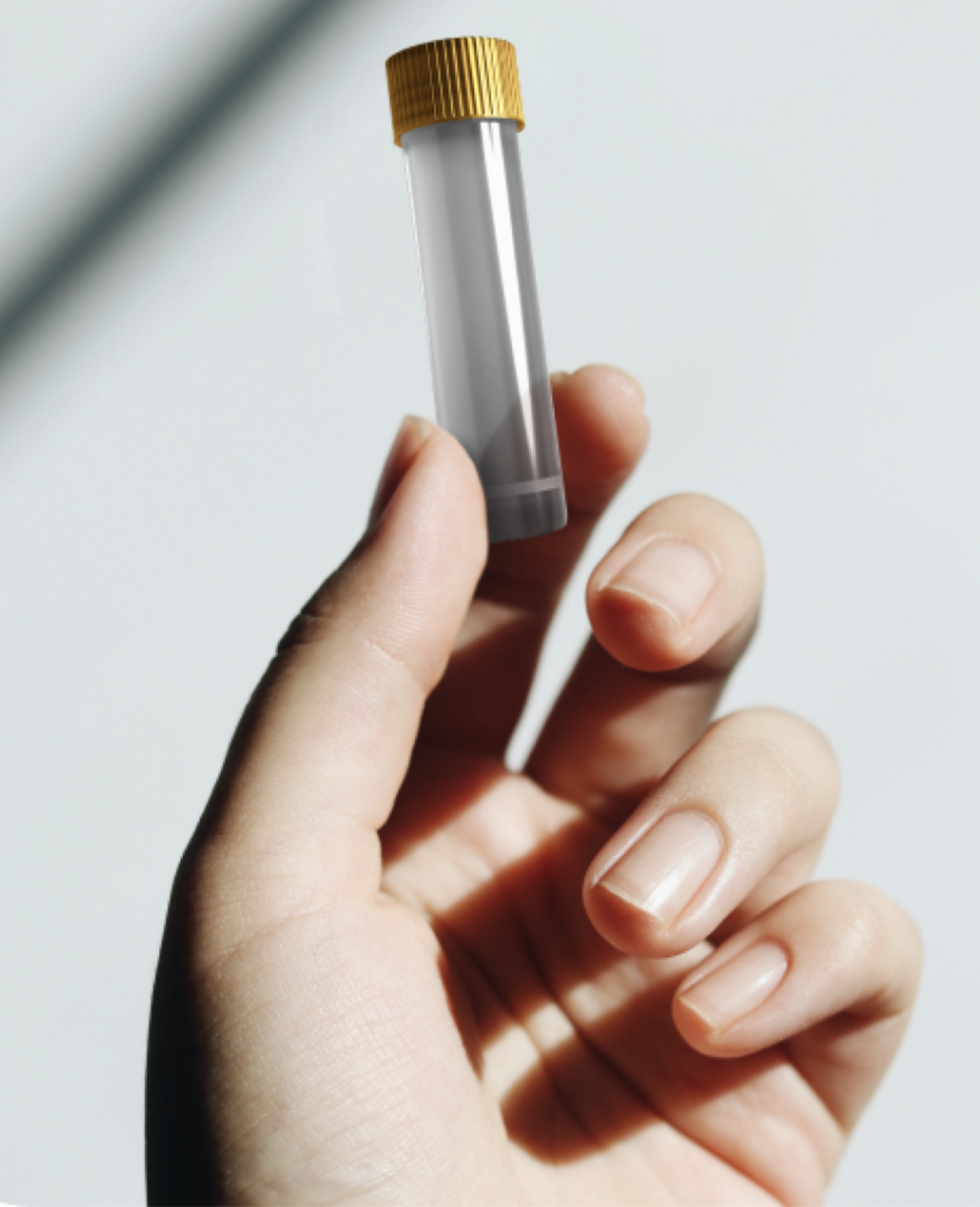 A hand holding a small, clear plastic vial with a yellow screw cap is displayed against a plain, light background—reminiscent of the minimalist designs often seen with massage guns and wellness tools.