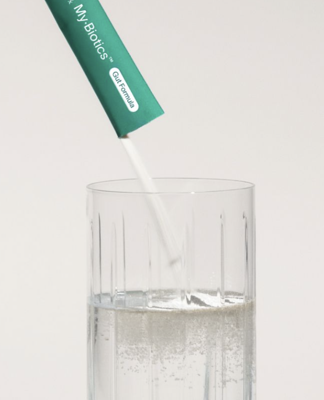 A packet labeled "MyBiotics Gut Formula" is being poured into a clear glass of water, with powder visible above the glass—perfect for those who value wellness, whether after a workout or using massage guns.