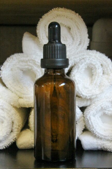 A brown glass dropper bottle is placed in front of neatly rolled white towels.
