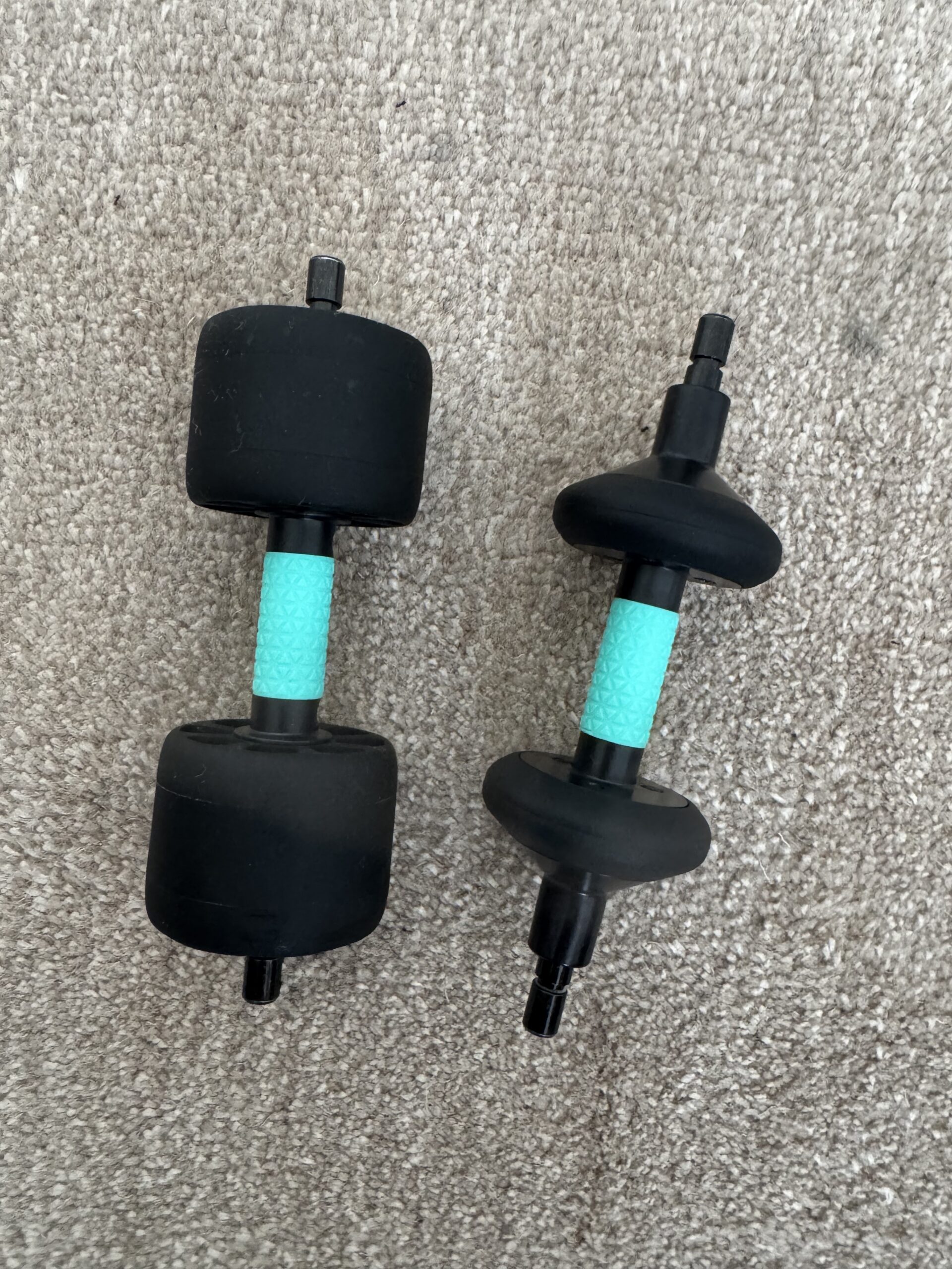 Two black and turquoise plastic objects with cylindrical and disc-shaped ends rest on a light brown carpet.