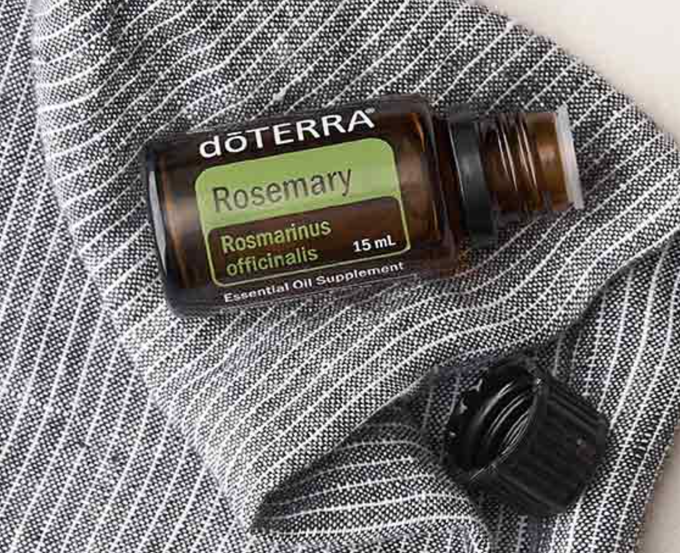 A 15 mL bottle of doTERRA Rosemary essential oil lies on a gray and white striped cloth, with the cap removed and placed nearby.
