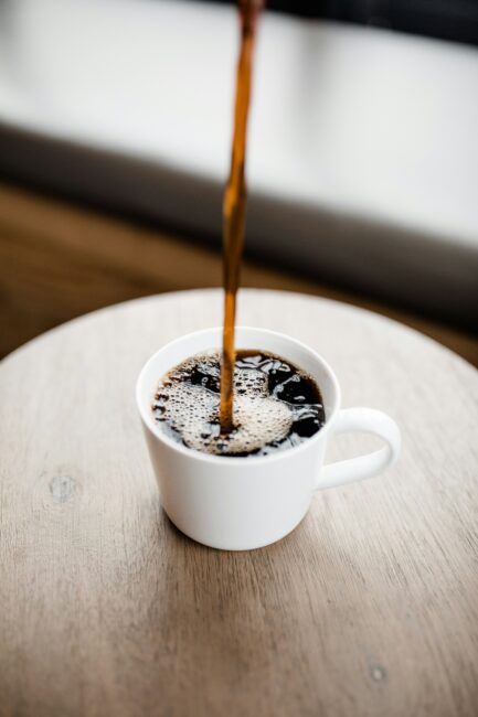 A stream of coffee being poured into a white mug on a wooden table.
