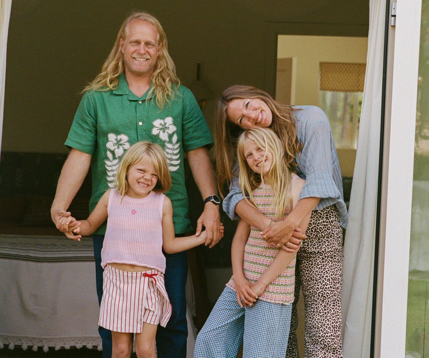 A family of four, two adults and two children, stand together in a doorway, smiling at the camera.