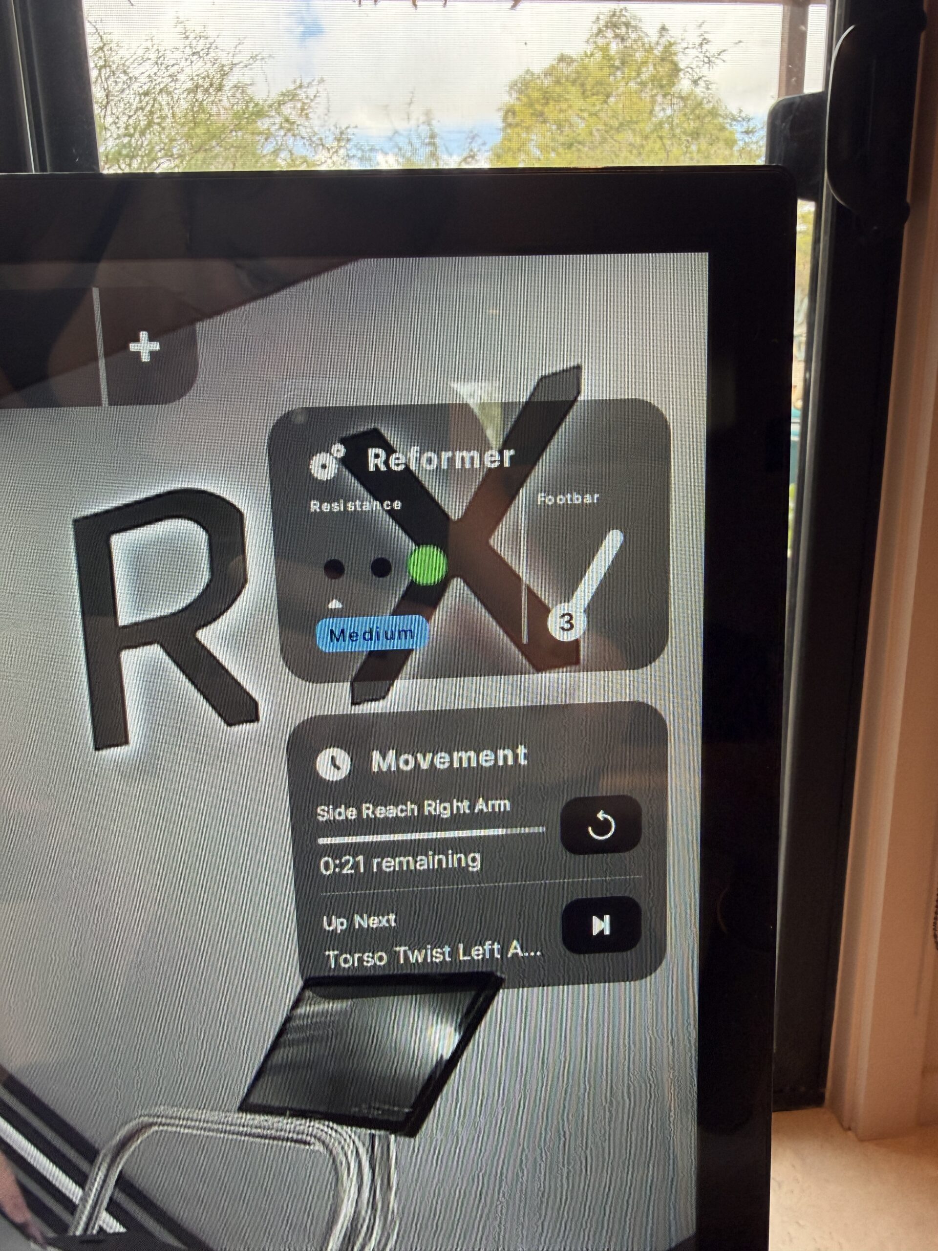 Digital display for a Pilates reformer showing medium resistance, footbar setting 3, and the current movement as “Side Reach Right Arm” with 21 seconds remaining.